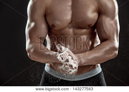 young muscular man preparing to hand lifting heavy weight. White talcum dynamically scatters in different directions. Close-up