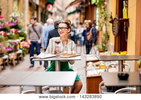 Young woman sitting at the cafe with shakerato coffee and panini outdoor on the famous street with local food markets in Bologna city.