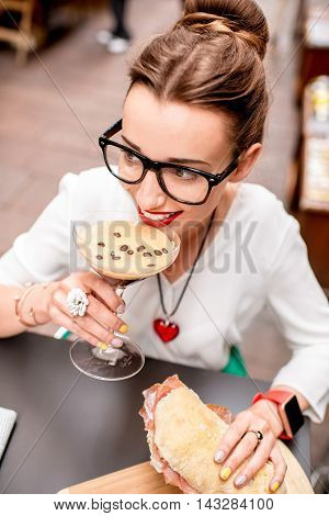 Young woman with shakerato coffee drink and panini with prosciutto outdoor.