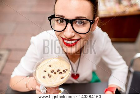 Young woman sitting at the cafe with shakerato drink in cocktail glass outdoor. Traditional italian cold coffee