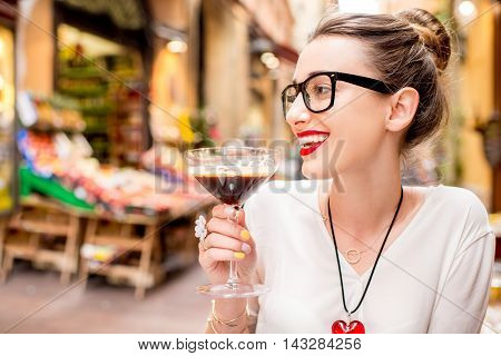 Young woman sitting at the cafe with shakerato drink in cocktail glass outdoor. Traditional italian cold coffee