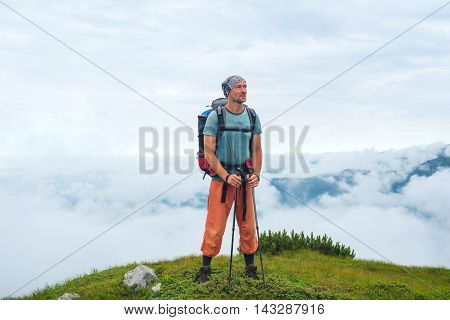 Smiling hiker with a backpack stands above the clouds on the top of the mountain. Beautiful day in the Carpathian mountains.