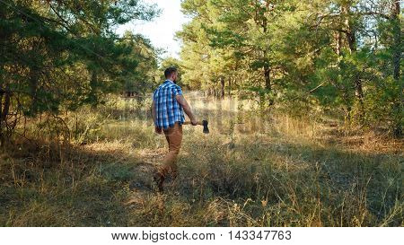 Lumberjack is in the woods holding the ax. A man in a plaid shirt. Hiking.