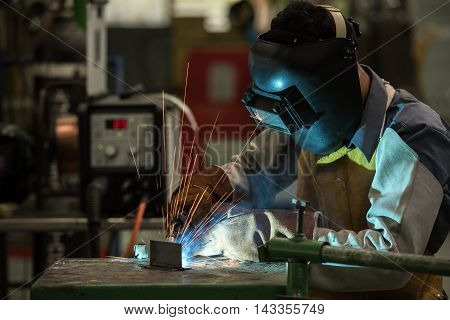 worker with protective mask welding metal and sparks in oil refinary plant.