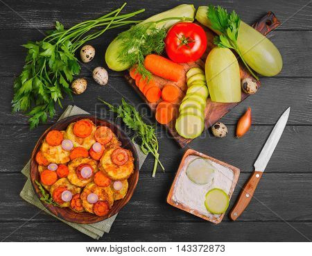 Vegetables ingredients for fried vegetable dishes in dough. Vegetables marrows white squashes carrots parsley lettuce dill tomato onions quail eggs flour. Black wood background.