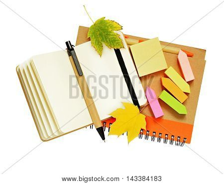 Notebook and pens with dry autumn leaves isolated on white