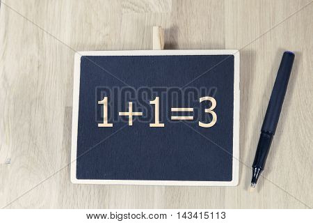 sentence 1+1=3 written with chalkboard on a table with pen.Business, technology, internet concept.