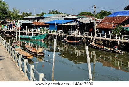 Samut Songkhram Thailand - December 29 2011: Old wooden fishing boats moored to walkways dock in front of a cluster of Thai houses at a small fishing village nestled on the banks of an estuary