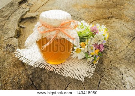 jar of honey on the stump with a bouquet of wild herbs