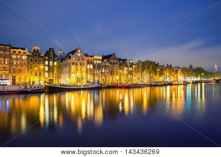 Night Amsterdam city view of Netherlands traditional houses with Amstel river in Amsterdam Netherlands