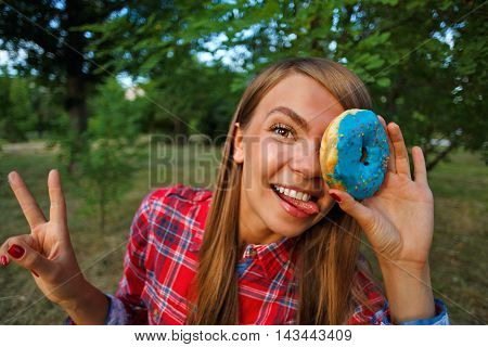 Funny girl holding a donut in hand closing one eye. Delicious.