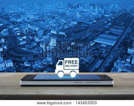 Free delivery truck icon on modern smart phone screen on wooden table over city tower street and expressway Transportation business concept