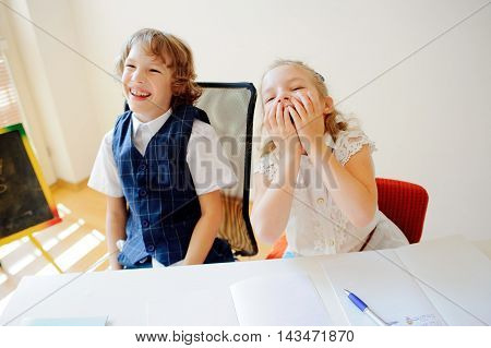 Funny little schoolchildren boy and girl sit at one desk. It's elementary school students. Children laugh. On the desk in children are school supplies and textbooks. Back to school.