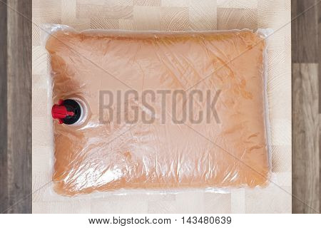 Plastic bag with tap full of apple juice on the wooden table