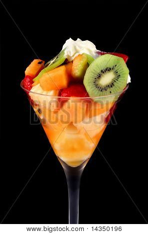 Verse fruitsalade en room in een hoog glas met zwarte achtergrond.