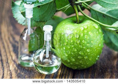 Apple vinegar in glass jar with ripe dreen fruit. Bottle of apple organic vinegar on wooden background. Healthy organic food.