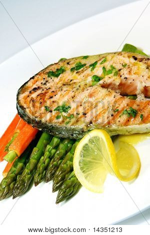 Dinner of grilled salmon steak with asparagus, baby carrots, a slice of lemon, and a butter and parsley sauce.