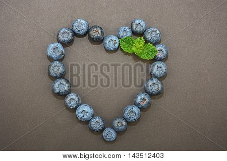 On a dark background  blueberries ligned up in the shape of a heart and decorated with mint leaf.
