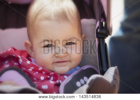 portrait of lovely and adorable baby girl sitting in stroller and smiling at camera in sunlight