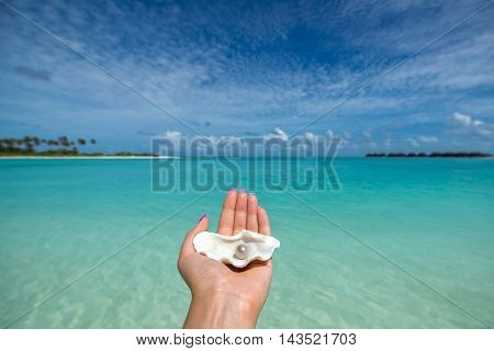 Open shell with a pearl on tropical beach in the woman's hand