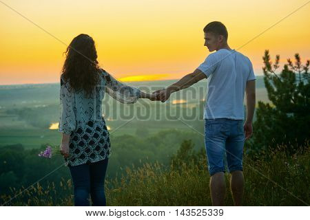 romantic couple walk at sunset on country outdoor, girl with bouquet of wild flower, beautiful landscape and bright yellow sky, love tenderness concept, young adult people