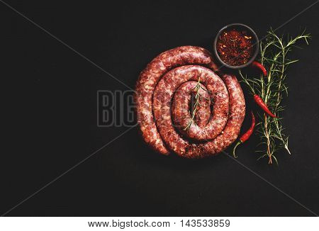 raw beef sausages on a cast-iron pan with rosemary and spices on a wooden table South African boerewors