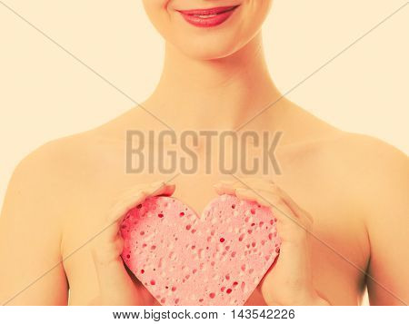 Skincare hygiene health and body treatment. Sensual naked woman with perfect skin holding orange heart shaped bath sponge in hands covering her breast. Toned image