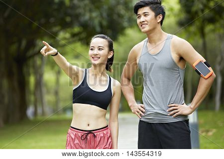 young asian couple exercising in park woman pointing at something in the distance.