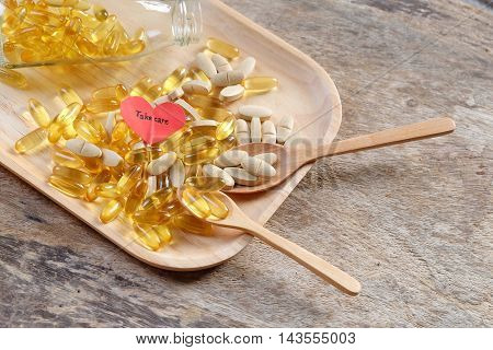 Supplement capsule dish on wooden background with red heart and take care wording.