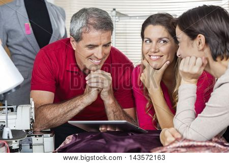 Happy Tailor Using Tablet Computer With Colleagues