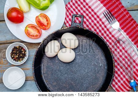 Fresh ingredients for omelet - three eggs in pot vegetables and spices on the wooden rustic table