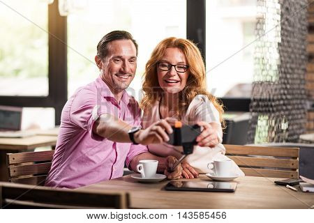 Photo together. Cheerful man and woman making selfie photos with the help of smart phone and selfie stick