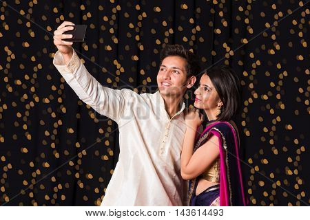 indian young Couple taking a self portrait or selfie using smart-phone in diwali festival