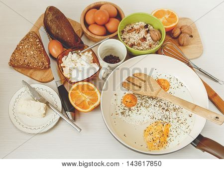 Fried Eggs in the Frying Pan,Breakfast Ingredients.Orange,Bread,Butter,Nuts,Porrige.Kitchen Accessories.Cooking Morning Food.White Table.