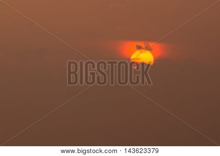 Close View Of Yellow Disk Of Setting Rising Sun With Red Glow Around, Partly Covered By Dark Clouds In Center, Brown Sky Background, Sunrise, Sunset, Dawn.