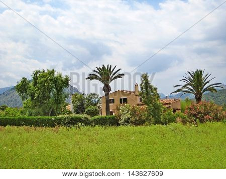 Pollenca Majorca Spain - June 28 2008: Finca vacation rental home with meadow on front surrounded by garden - tramuntana mountains in background