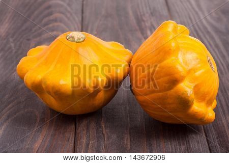 two yellow pattypan squash on a dark wooden table.