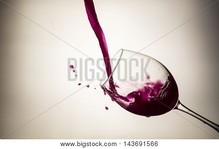 Red wine pouring in a wineglass with wine drops on light background