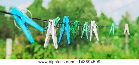 Plastic clothespins laundry hook colorful rope.Village plastic pegs. Three white clothes pins two blue clothespin rope on focus four green clothespins. Summer rural landscape.