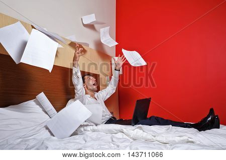 To hell with the job. Businesswoman throws documents. Man with laptop sitting on the couch and fly papers around him. Deadline. Dash it!