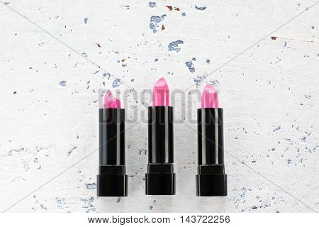Pink lipstick in black container set, flat lay, copy space. Three new rosy rouge lying on white textured background. Female decorative cosmetic, make-up, beauty concept
