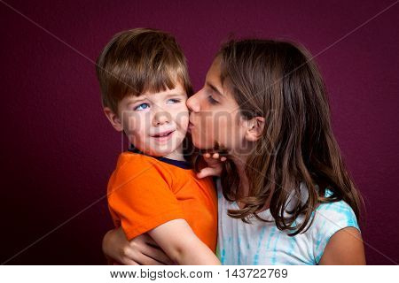 A little boy looks repulsed as he tries to recoil from a kiss his older sister is giving him.