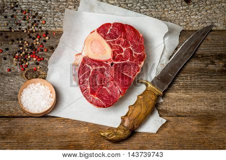 Raw fresh cross cut veal shank and meat cleaver for making Osso Buco on wooden background, top view