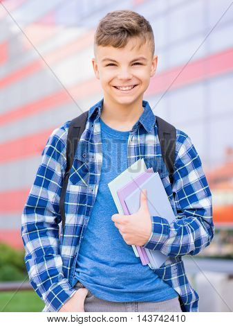 Happy teen boy holding books on the first school day. Outdoor portrait. Young student beginning of class after vacation. Back to school concept.