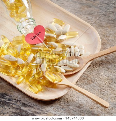 Supplement capsule dish on wooden background with red heart and take care wording.