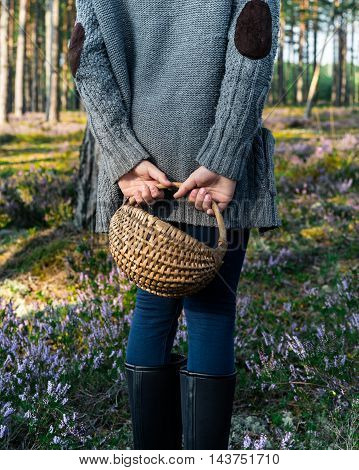 Girl standing back to camera in the forest and holding a basket. Mushroomer.
