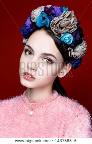 Beautiful model with a wreath of flowers on her head on red background