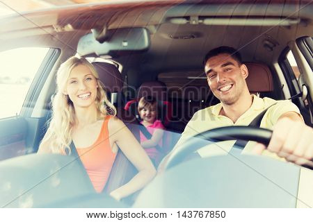 family, transport, safety, road trip and people concept - happy man and woman with little child driving in car
