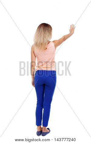 Back view of beautiful woman welcomes. Young teenager girl in jeans hand waving from. Rear view  people collection.  backside view of person.  Isolated over white background. Blonde in blue pants