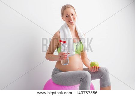 Pregnant woman drinking water after workout and holding apple in her hand